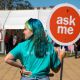 Student ambassador wearing a turquoise t-shirt and matching hair holds an orange round sign that reads 