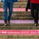 Two people walk down steps with welcome messages in multiple languages on the risers