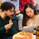 Two young people read a document whilst eating pizza.