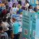 Busy Welcome Week event with students and staff at informational booths, featuring banners for University of Sussex Wellbeing and IT Services.