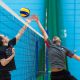 Two volleyball players jump to reach for the ball at the net