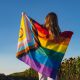 A woman faces away from camera with the progress pride flag across her shoulders