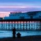 The silhouettes of two people on the beach looking out at Brighton pier at sunset