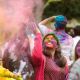 Group of students joyfully celebrating Holi, their faces and clothes covered in vibrant colors. They are laughing and throwing coloured powder into the air, creating a cloud of hues.