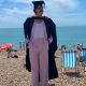 Pablo Santana in graduation clothing on the Brighton Beach with deck chairs and people in the background