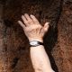 A hand wearing a rock reaches to touch the bark of a tree
