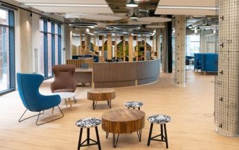 A modern space with a semi-circular reception desk, some stools and couple of armchairs around low coffee tables.