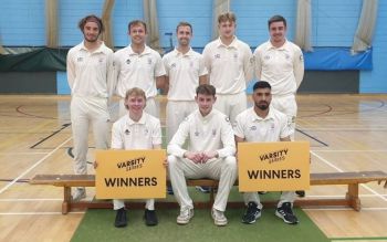 The cricket team in their white uniforms sitting on a bench and holding two yellow signs saying 