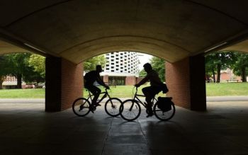 Two men cycling in opposite directions under the arches of Pevensey 1. The light comes from behind them, where the Meeting House is
