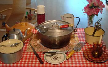 old fashioned plates and cooking tools on top of a table covered with a red and white chequered tablecloth. The decoration includes a thermo and some plastic flowers on a vase.