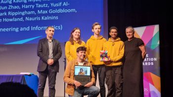 Education Award group of winners posing for a photo, one holding a laptop screen showing another winner on a Zoom call