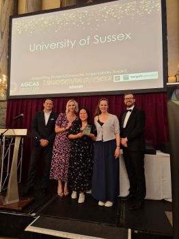 Members of the CEE team stand on stage at the AGCAS awards ceremony, holding a certificate. Behind them is a large screen displaying “University of Sussex Supporting Student/Graduate Employability Award AGCAS winner”