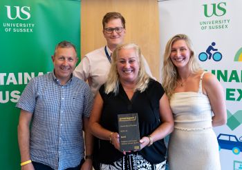 Members of the BSMS Green Impact team stood together with their recycled slate gold award in front of Sustainable Sussex banners