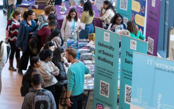 Busy Welcome Week event with students and staff at informational booths, featuring banners for University of Sussex Wellbeing and IT Services.