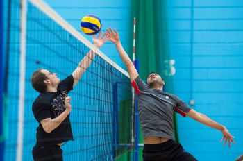 Two volleyball players jump to reach for the ball at the net