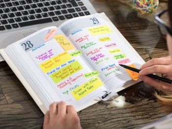 A person updates their diary, which is full of text in different colours and post-it notes.