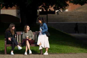 Three students talking on a bench by Library Square