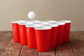 Red cups set up in a triangle shape on a table top for drinks pong, a table tennis ball hangs in mid-air