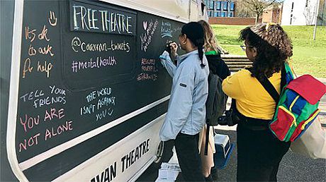Students write on a chalk board as part of the Caravan Theatre on campus