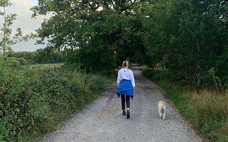 Student walking a dog in the countryside, seen from behind