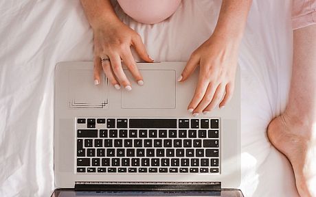 Woman sitting on bed using laptop