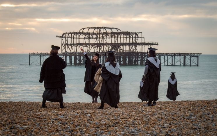 Six students wearing their graduation gowns at the beach in front of the West Pier