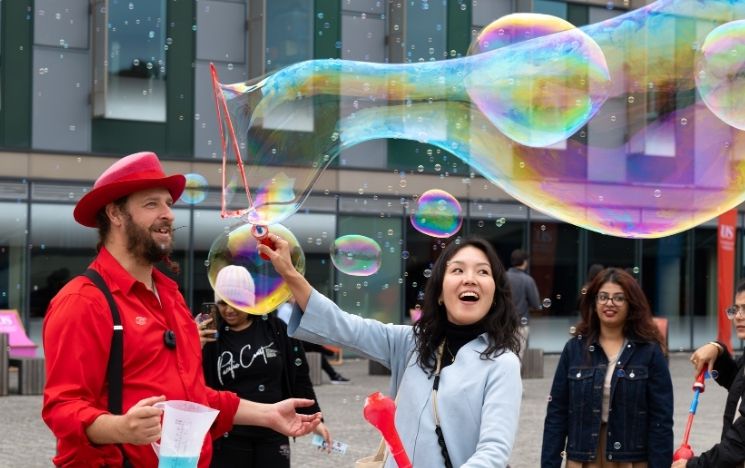 Students smile as one student makes a large bubble from a bubble wand.