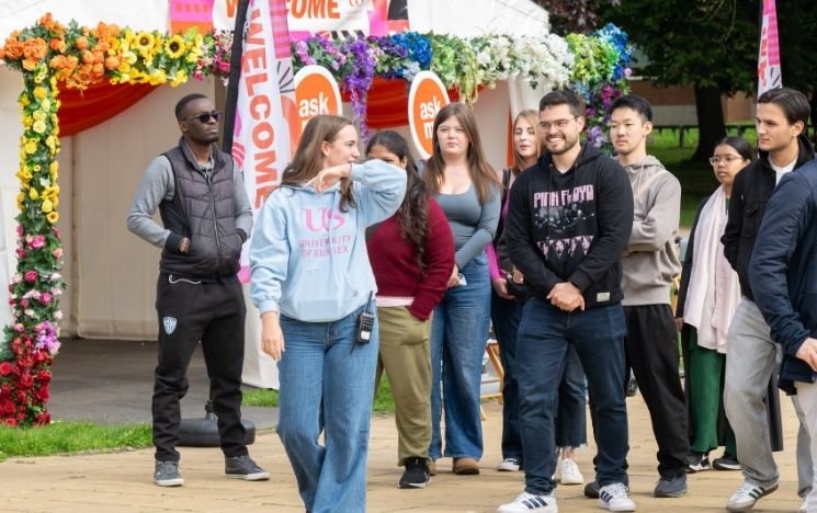 A group of students walk past the Welcome marquee in library square, following a welcome week student ambassador.