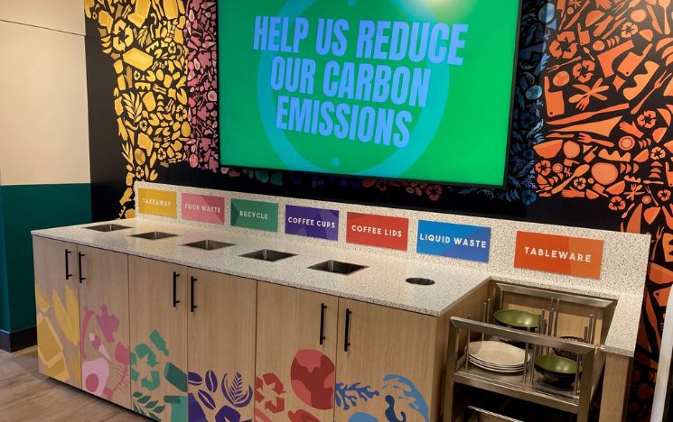 Recycling bin station with a big screen that displays the message "Help us reduce our carbon emissions"