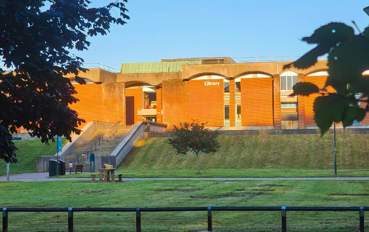 Photo of the Library through the trees on campus