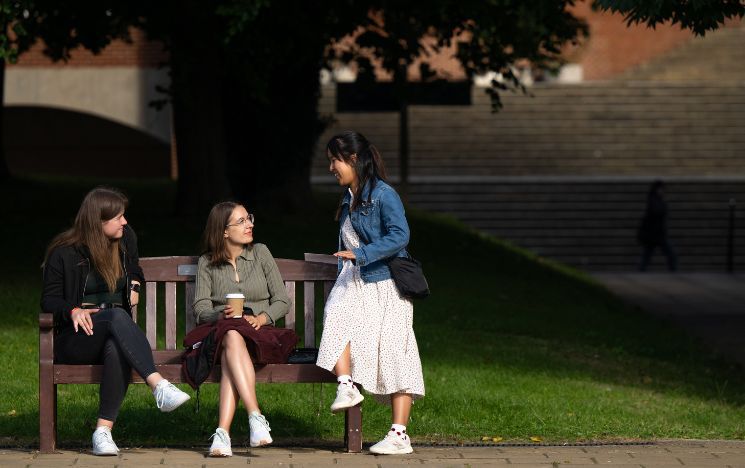 Three students talking on a bench by Library Square