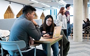 Two students discuss some work at a table inside the Student Centre