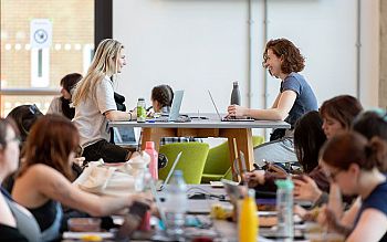 Two young women share a joke amongst a large gathering of students working in the Student Centre