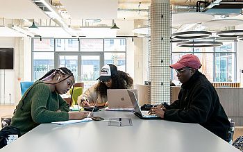 Three students at a table with laptops and notebooks inside the Student Centre