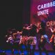 Students dancing in a line on the stage of the Attenborough Centre for the Creative Arts. Behind, a partial text reads Caribbean Stu Unite