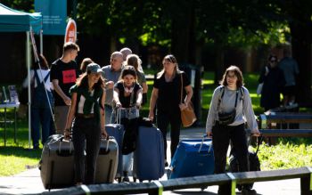 Group of students pushing their heavy suitcases across campus