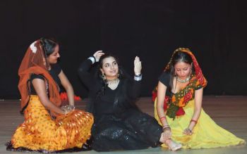 Three young women dressed in traditional Indian clothes performing on stage
