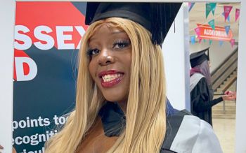 Black female student posing on her graduation gown in front on the SoSA stall at the winter graduation