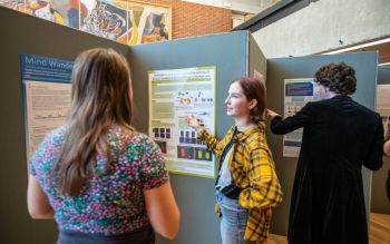 Female student explaining her research to another student in front of her poster