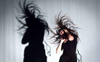 Woman dancing. Her shadow is projected on the white curtain that covers the back of the stage
