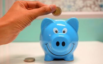 Hand inserting a coin in a blue piggy bank