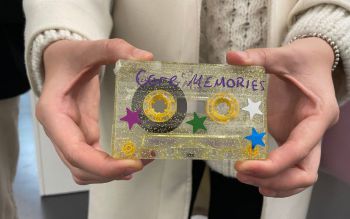 Two hands holding a cassette tape decorated with glitter, stars and the text 'core memories'