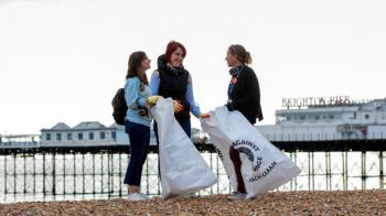 Three students collect plastic on the beach near the Pier