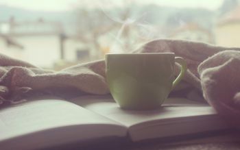 A cup of tea resting on a book, surrounded by a blanket